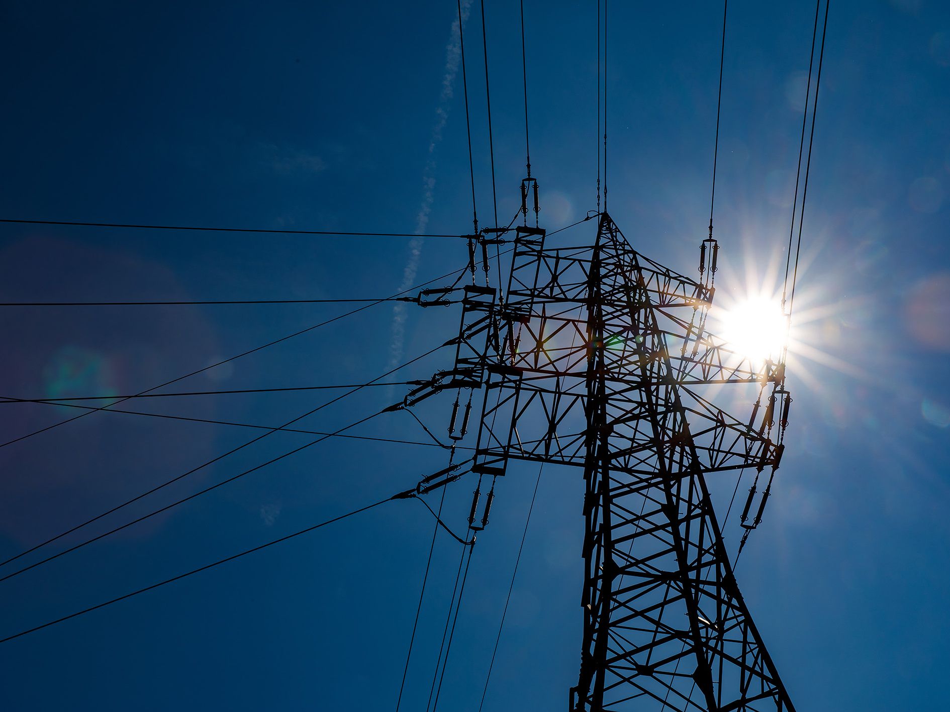 Strommasten vor blauem Himmel und Sonne