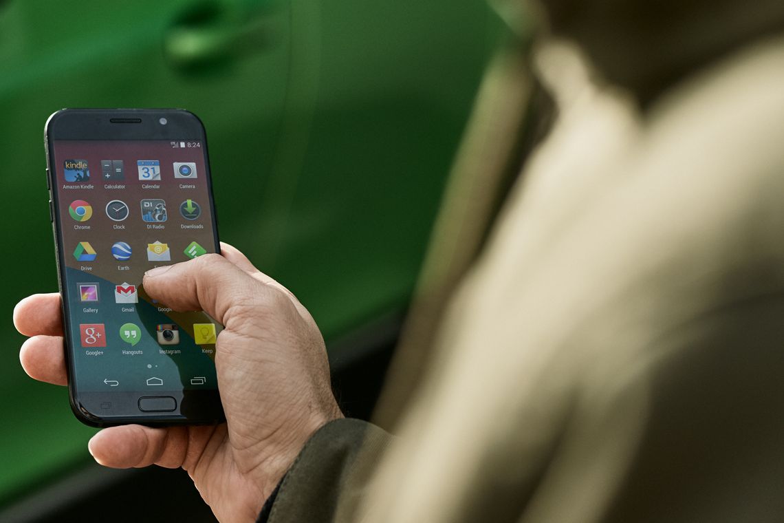 Handy in der Hand im Vordergrund, E-Auto im Hintergrund