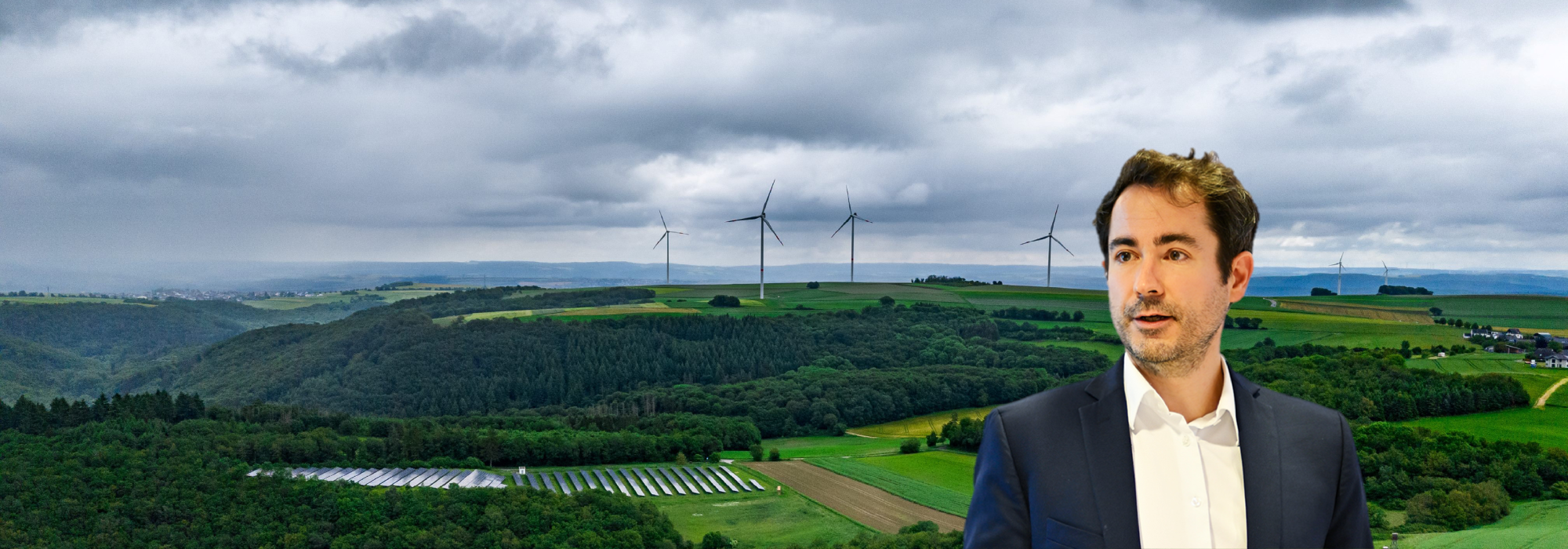 Dr. Anton Burger auf der rechten Seite und im Hintergrund sieht man eine Waldlandschaft und Windräder 